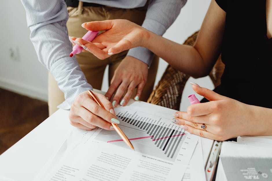 Two individuals collaborating on business chart analysis with markers in an office setting.